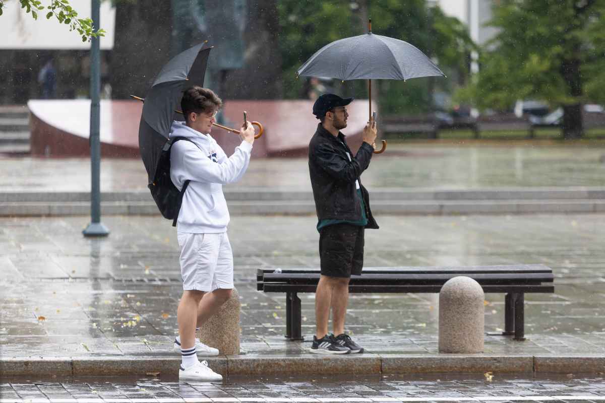 Du vyrai laiko atvirus skėčius ir žiūri į telefonus lietingą dieną.